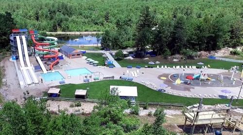 Aerial view of a water park featuring slides, a pool, and a splash pad surrounded by greenery.