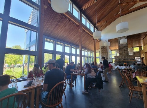 A bright, modern restaurant interior with large windows, wooden tables, and patrons enjoying their meals.