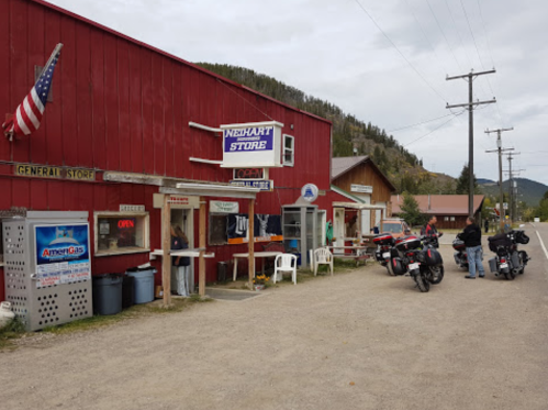 A red general store with an American flag, motorcycles parked outside, and a small town street in the background.