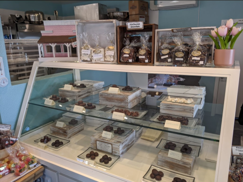 A display case filled with assorted chocolates and confections, with decorative packaging and a vase of tulips nearby.