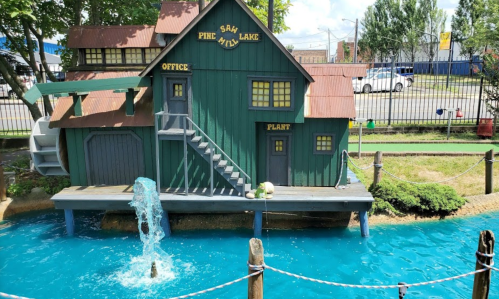 A miniature green building with a water feature, labeled "Pine Lake," surrounded by blue water and greenery.