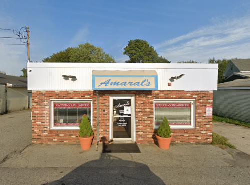 A brick building with a sign reading "Amaral's," featuring seafood and sandwich offerings, under a clear blue sky.