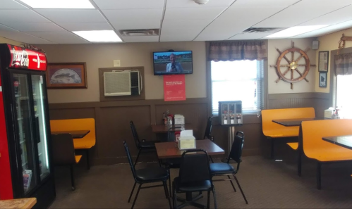 Interior of a casual dining area with orange booths, tables, a TV, and a Coca-Cola vending machine.