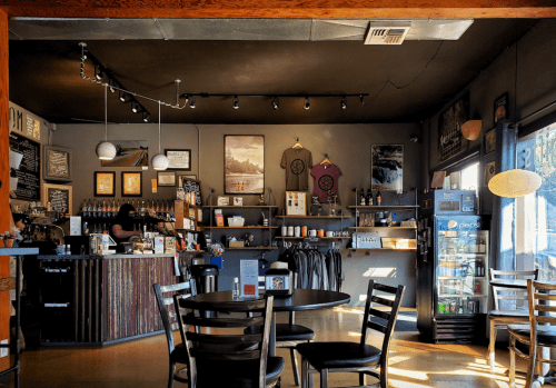 Cozy café interior with a counter, shelves of products, and tables. Warm lighting and a relaxed atmosphere.