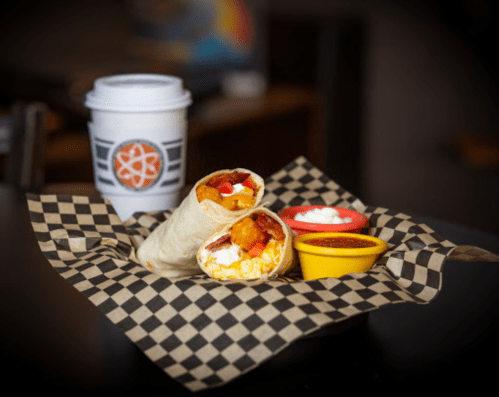 A plate with two burritos, one with toppings, and two dipping sauces, alongside a coffee cup on a checkered paper.