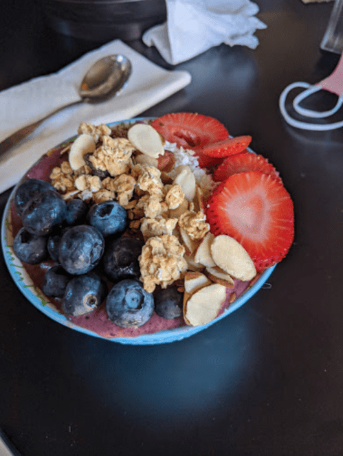 A colorful bowl of smoothie topped with blueberries, strawberries, granola, and sliced almonds on a black table.