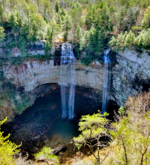 Aerial view of a stunning waterfall cascading into a rocky pool, surrounded by lush green trees and cliffs.