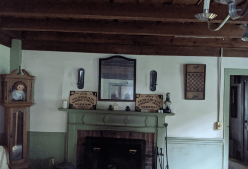 A cozy room with a fireplace, vintage decor, a mirror, and a chessboard on the wall.