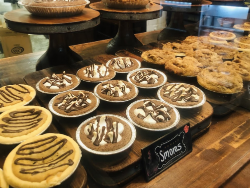 A display of various mini pies, including s'mores and other desserts, on wooden stands in a cozy setting.