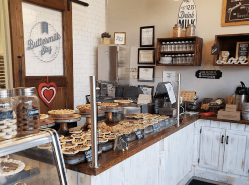 A cozy bakery display featuring various pies and desserts, with a welcoming sign and rustic wooden decor.