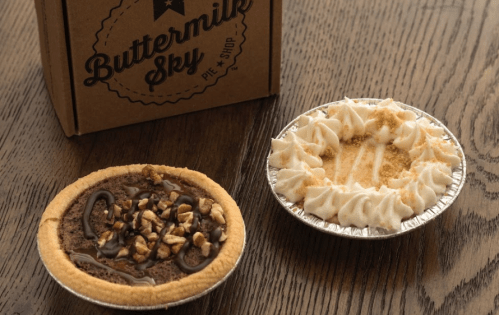 Two delicious pies on a wooden table: one chocolate with nuts and one creamy pie with whipped topping and graham cracker crumbs.