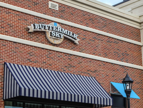 Sign for Buttermilk Sky Pie Shop on a brick building, featuring a striped awning and a decorative lamp post.