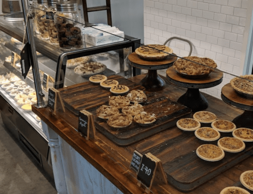 A display of various baked goods, including pies and cookies, on wooden stands in a cozy bakery setting.