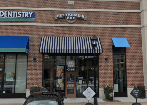 Exterior of Buttermilk Sky Pie Shop with a striped awning, surrounded by shops and planters, labeled "Closed."