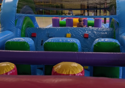 A colorful inflatable play structure with various shapes and obstacles, featuring a child playing inside.