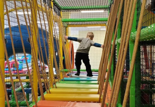 A child balances on colorful steps in a play structure, surrounded by netting and vibrant colors.