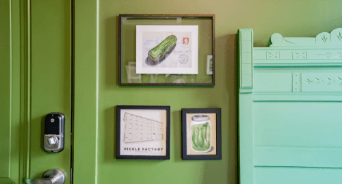 A green wall featuring framed pickle-themed artwork and a door handle.