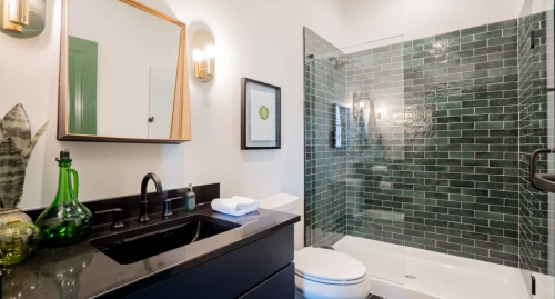 Modern bathroom featuring a black vanity, green tile shower, and stylish decor.