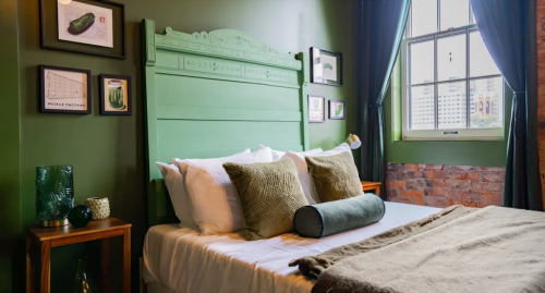 Cozy bedroom with a green headboard, decorative pillows, and a window, featuring a warm, inviting atmosphere.