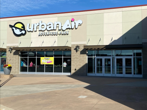 Exterior of Urban Air Adventure Park, featuring a colorful sign and large glass entrance on a sunny day.
