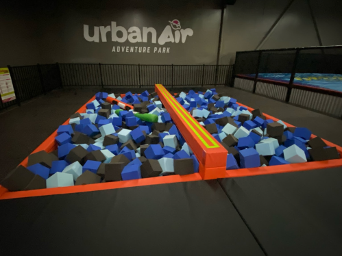 A foam pit filled with blue and black cubes at Urban Air Adventure Park, with a balance beam in the center.