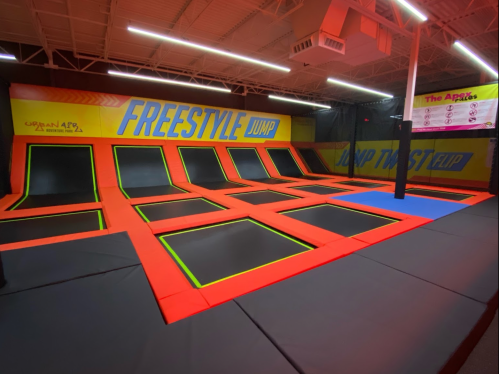 A spacious indoor trampoline park with multiple trampolines and vibrant orange and yellow walls.