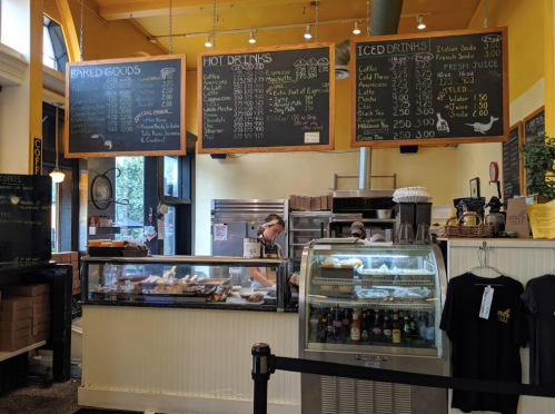 A café counter with a menu board, baked goods display, and staff preparing drinks in a bright, inviting space.