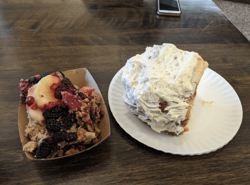A dessert plate featuring a berry crumble and a large slice of cake with white frosting on a paper plate.