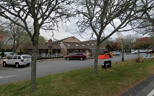 A quaint storefront with outdoor seating, surrounded by trees and autumn leaves, on a cloudy day.