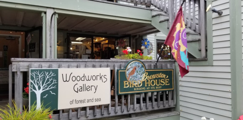 Exterior view of Woodworks Gallery and Brewster Bird House, featuring signs and colorful decorations.