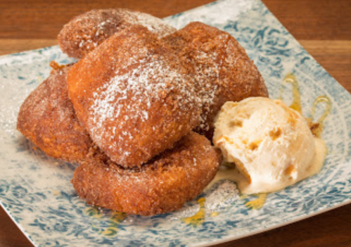 A plate of golden-brown fried pastries dusted with powdered sugar, served with a scoop of vanilla ice cream.