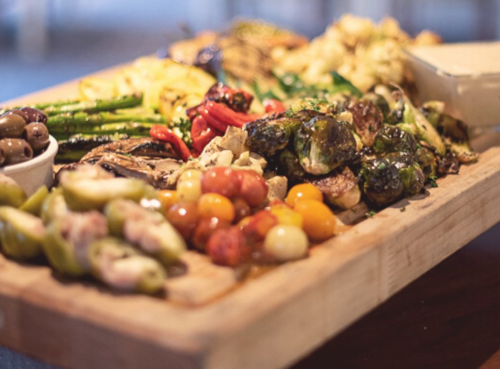 A wooden platter filled with grilled vegetables, olives, and a creamy dip, showcasing vibrant colors and textures.