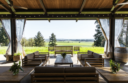 A spacious outdoor seating area with wooden furniture, overlooking a lush green landscape and distant trees.