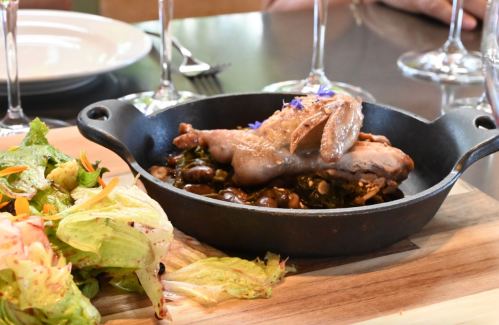 A cast iron skillet with cooked chicken, beans, and greens, accompanied by a fresh salad on a wooden board.