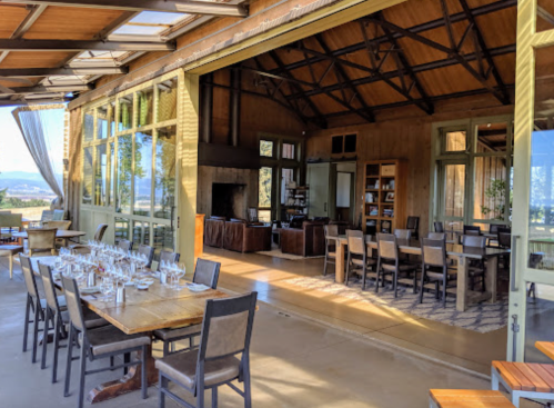 A spacious dining area with large windows, wooden tables, and chairs, overlooking a scenic view.