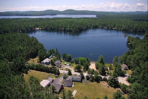 Aerial view of a serene lake surrounded by lush greenery and a small community of houses along the shore.