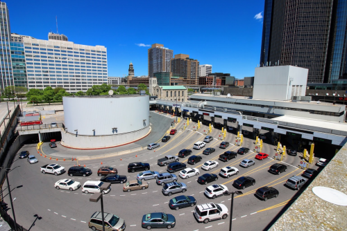 A busy urban toll plaza with cars lined up, surrounded by tall buildings and a clear blue sky.
