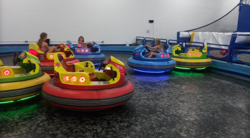 Children enjoying bumper cars in a colorful indoor amusement area. Bright lights and playful atmosphere.