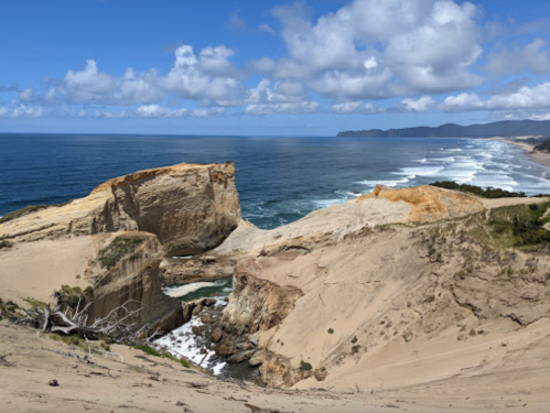 A scenic coastal view featuring cliffs, sandy shores, and waves under a partly cloudy sky.