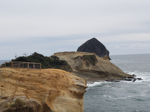 A rocky coastline with a prominent peak rising from the ocean under a cloudy sky.