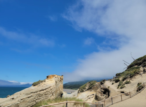 A sandy beach with rocky formations under a blue sky, partially covered by clouds.