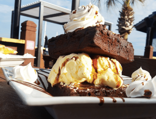 A decadent dessert featuring a brownie topped with ice cream, whipped cream, and chocolate drizzle on a plate.