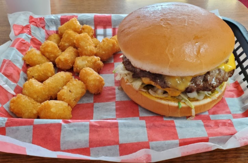 A cheeseburger with lettuce and a side of golden tater tots on a red and white checkered tray.