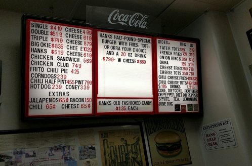 Menu board featuring various burgers, sandwiches, sides, and drinks with prices listed, including Coca-Cola branding.