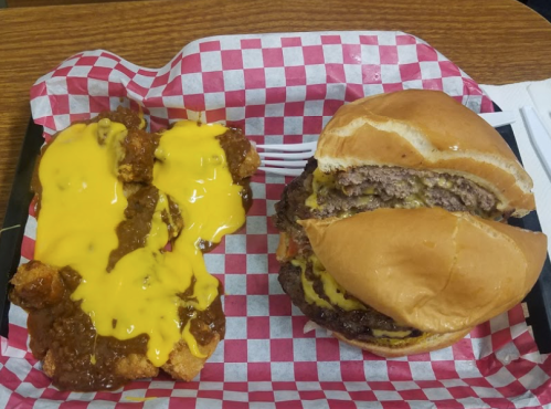 A plate with a cheeseburger and a side of chicken topped with melted cheese and chili, served on a checkered tray.