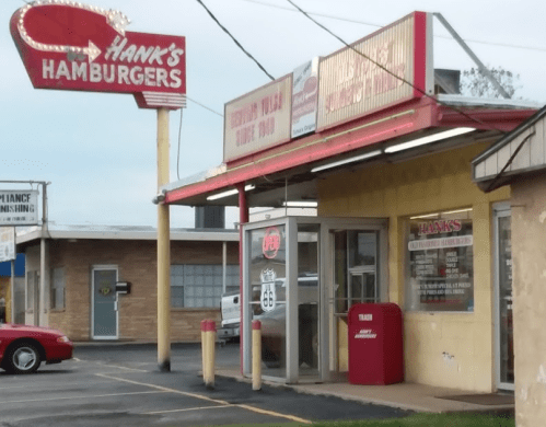 A retro diner named Hank's Hamburgers with a neon sign, featuring a red mailbox and Route 66 signage outside.