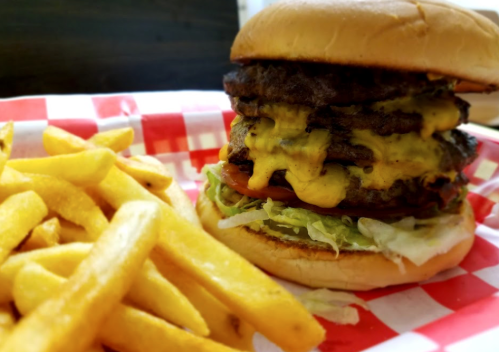 A towering cheeseburger with multiple patties, melted cheese, lettuce, and tomato, served with golden French fries.