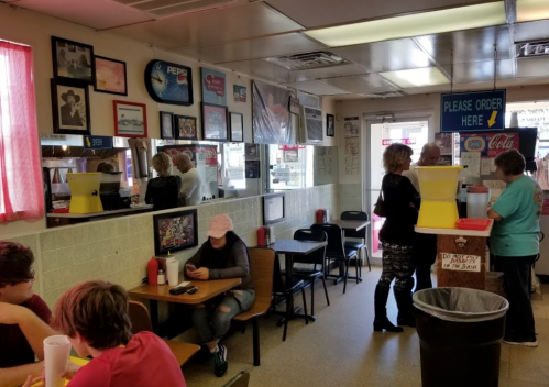 A casual diner interior with patrons at tables, a counter, and colorful decor, including mirrors and posters.