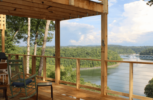 A wooden deck overlooks a river and lush green hills under a partly cloudy sky.