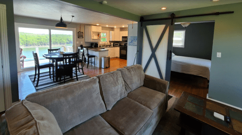 Cozy living space with a sofa, dining area, kitchen, and a view of a lake through large windows.